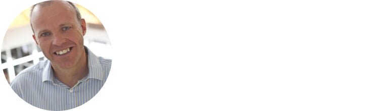 Chris wears a blue collar shirt and is smiling