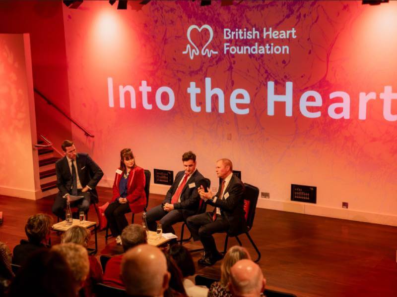 3 panel speakers sit on stage in front of a red backdrop which reads "Into the Heart"