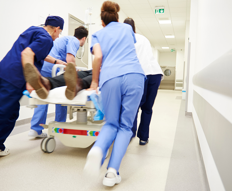 Doctors rushing down a hospital hallway with a patient in a bed suffering from a cardiac arrest
