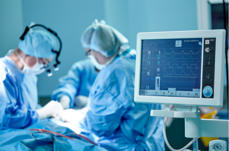 A heart pressure monitor and 2 doctors performing surgery in an operating room