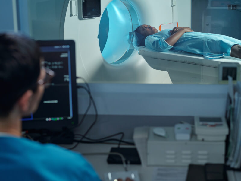 Person entering MRI scan machine with doctor looking at a computer screen to monitor the scan