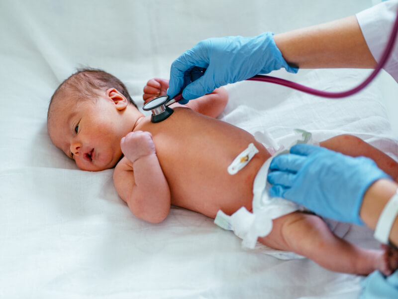 Newborn baby lying down as a doctor with blue gloves checks their heartbeat 