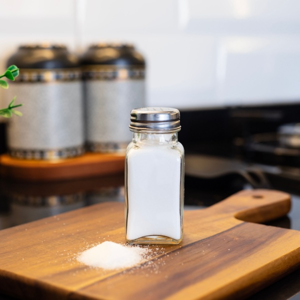 Salt shaker on a wooden chopping board, next to a pile of salt