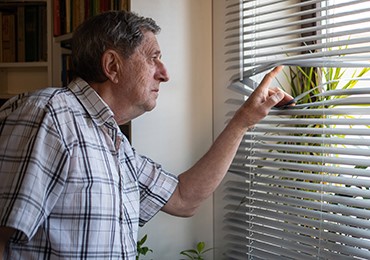 Man looking through his window blinds