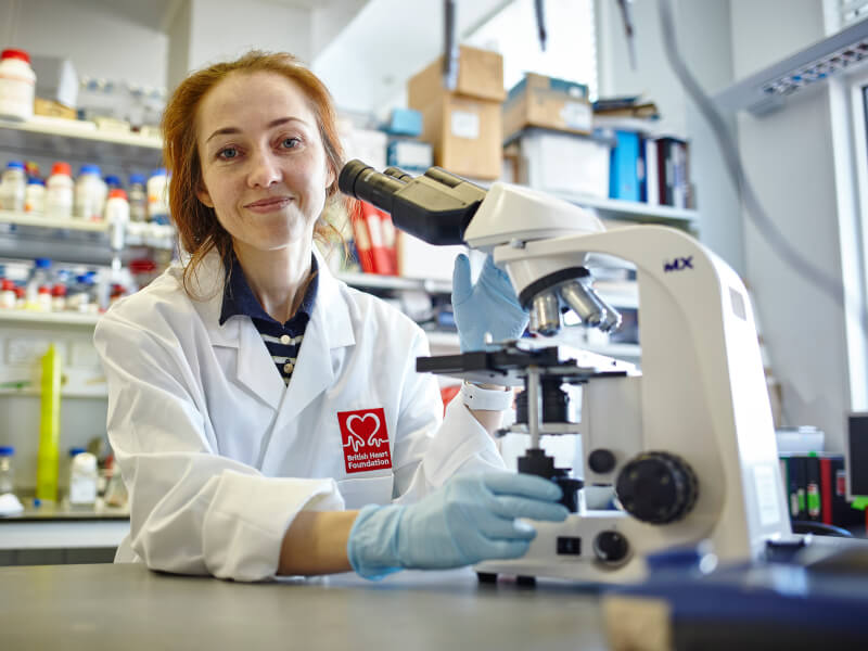 Researcher in a lab sat at a desk with a microscope in front of her