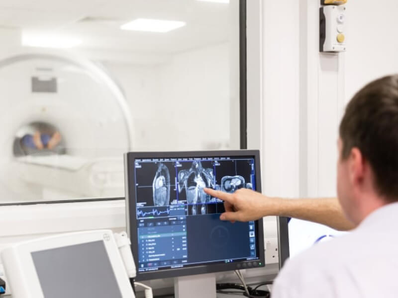 Two people are looking at an MRI scan with an MRI machine visible through the window