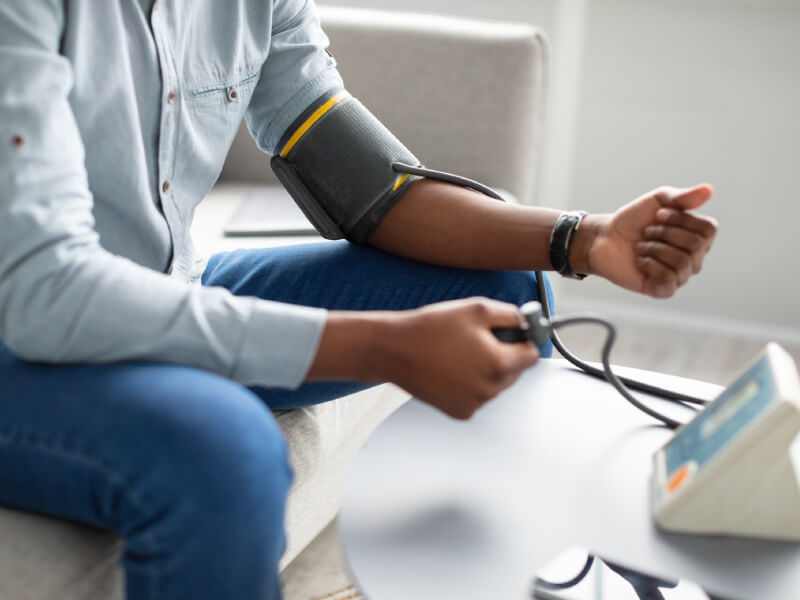 A man sits on a sofa and takes a blood pressure reading