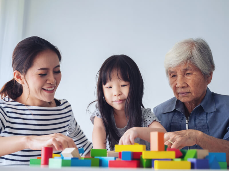A young daughter, mother and grandmother sit at a table and play with children's toys