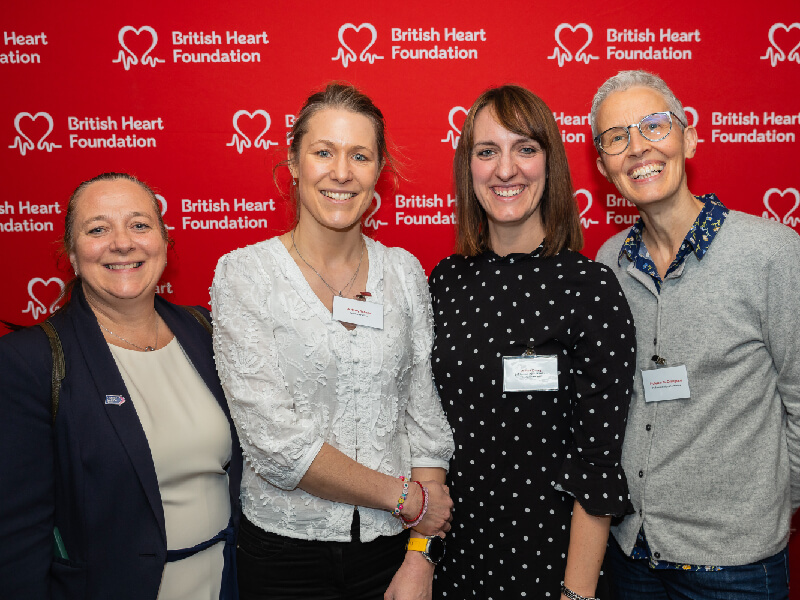 4 women pose for a photograph with a red background featuring BHF's logo