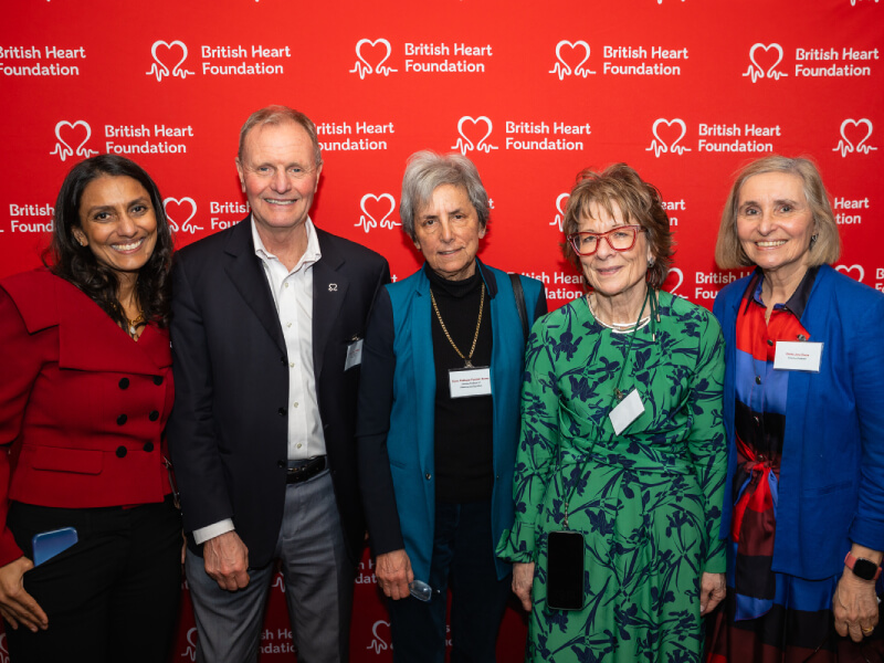5 people pose for a photograph with a red backdrop featuring the BHF logo