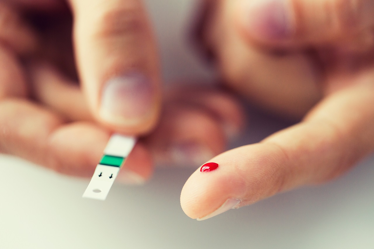 Close up of a finger holding a drop of blood and a test strip