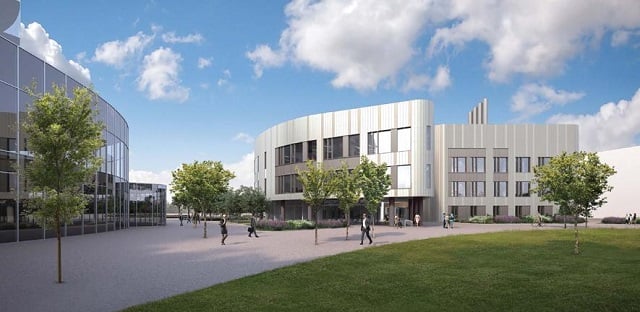 The Heart & Lung Research Institute (HLRI) in Cambridge: a modern glass building next to a silver building with some grass and trees beside and people walking.