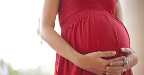 Pregnant woman wearing red dress holds her baby bump