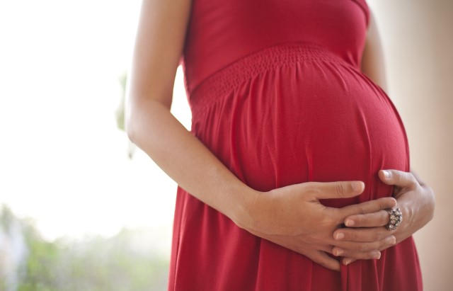 Pregnant woman wearing a red dress holds her baby bump