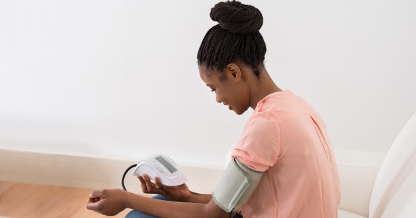 A woman sitting on a sofa measures her blood pressure using a home blood pressure monitor