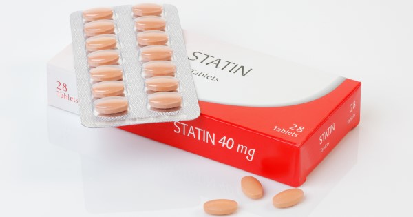A photograph of a packet of statins, with one strip of tablets sat on top of the box and 3 single tablets next to the box