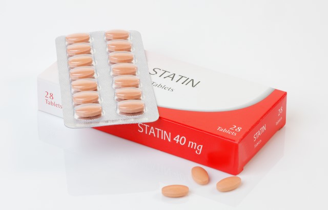A photograph of a packet of statins, with one strip of tablets sat on top of the box and 3 single tablets next to the box