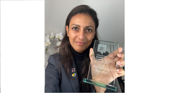 Dr Sonya Babu-Narayan holds up an Inspiring Communicator award made of glass. An orchid is in the background