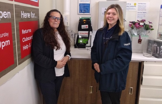 Two women stand in front of a life saving defibrillator in a Tesco Express store