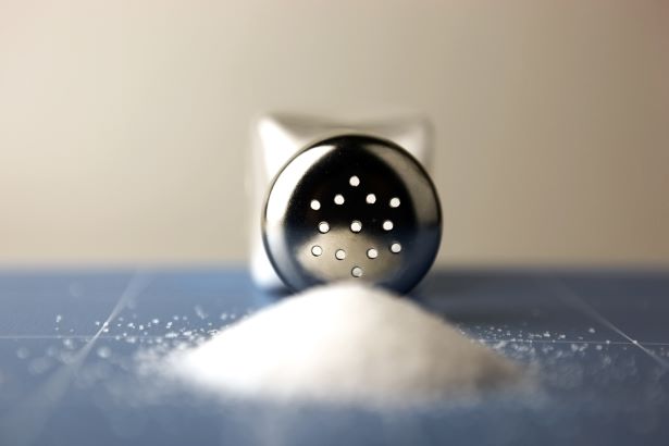 A salt shaker on its side next to a pile of spilled salt. 