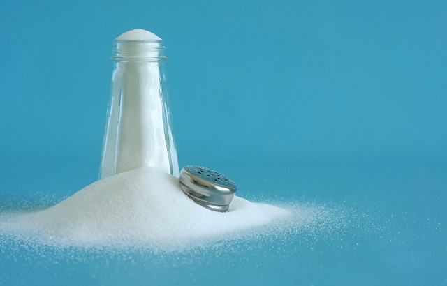 A salt shaker overflowing with salt on a blue background