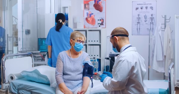 A photograph of a woman wearing a face covering having her blood pressure measured