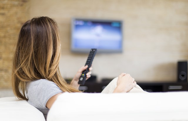 Photograph of a woman sat on a sofa watching TV