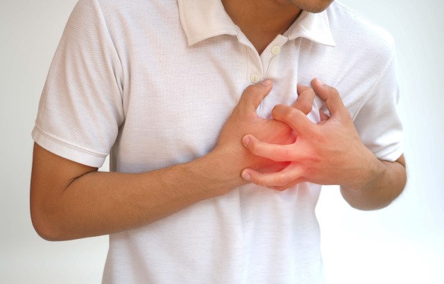 A man wearing a white polo shirt clutches his chest in pain