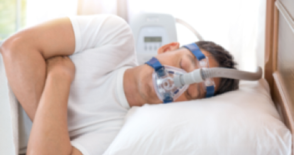 A man lying asleep on his side in bed wearing a CPAP machine for sleep apnoea