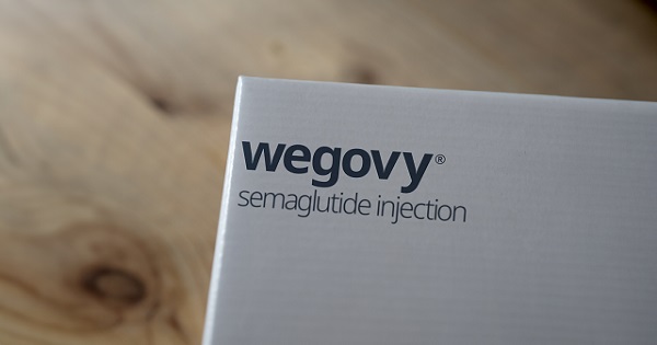 A stock image showing part of a white box with 'wegovy - semaglutide injection' written in blue. The background is faded out but appears to be an oak surface