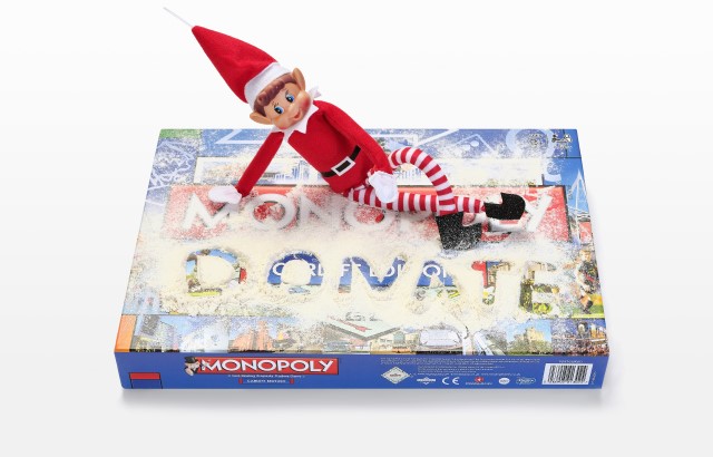 A Christmas elf sat on a dusty Monopoly game with 'Donate' written into the dust.