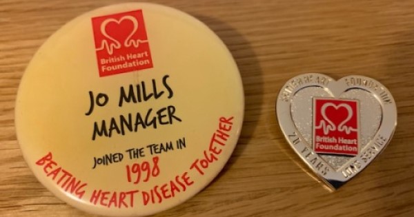 Two badges on a surface. One reading 'Jojo Mills, Manager, joined the team in 1998, beating heart disease together'. The second reading 'British Heart Foundation, 20 years long service.'