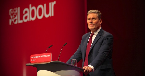 Keir Starmer. Leader of the Labour party, stands at a conference stand against a red background