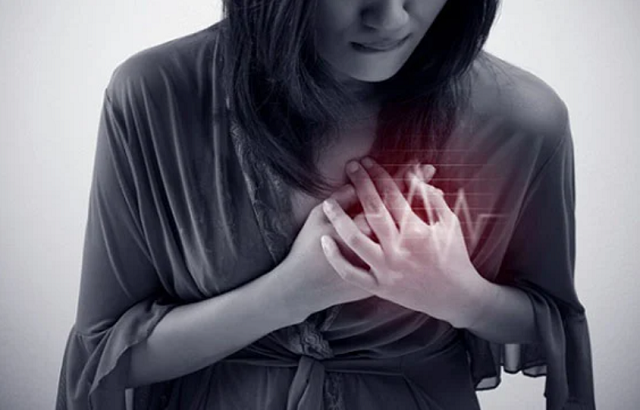 A woman in black and white clutches her chest which is glowing red