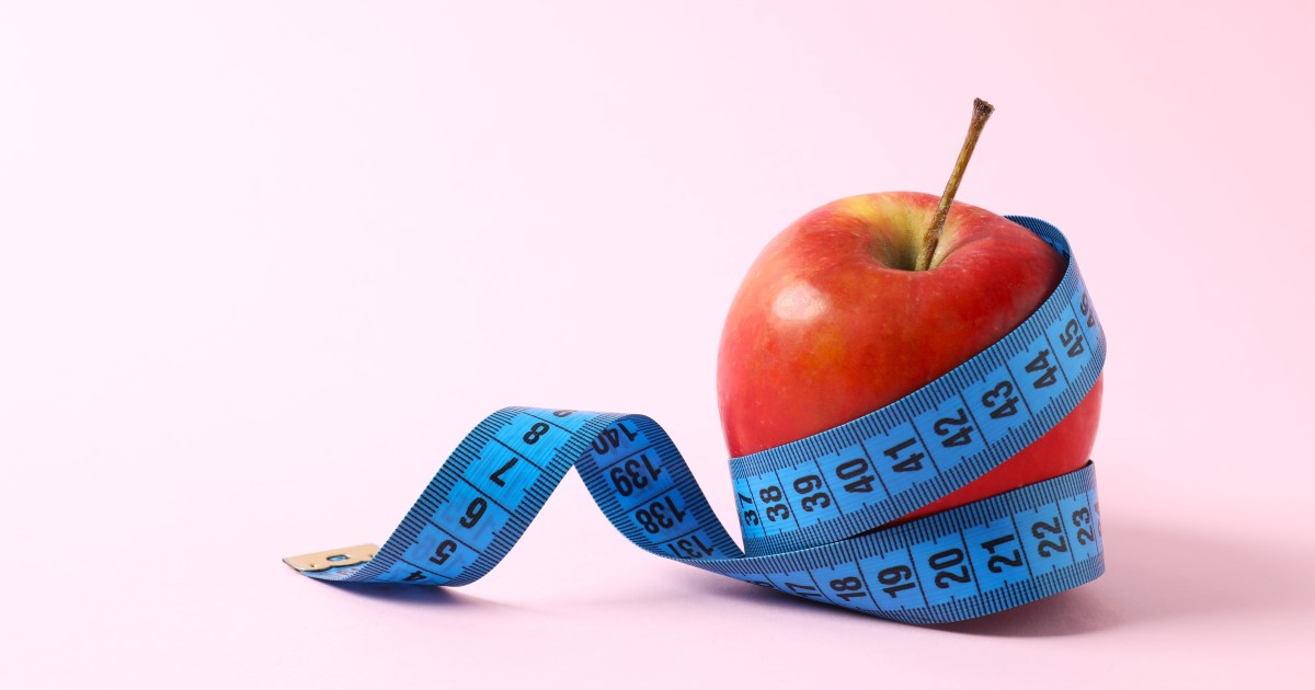 A photograph of a red apple with a blue measuring tape wrapped around it