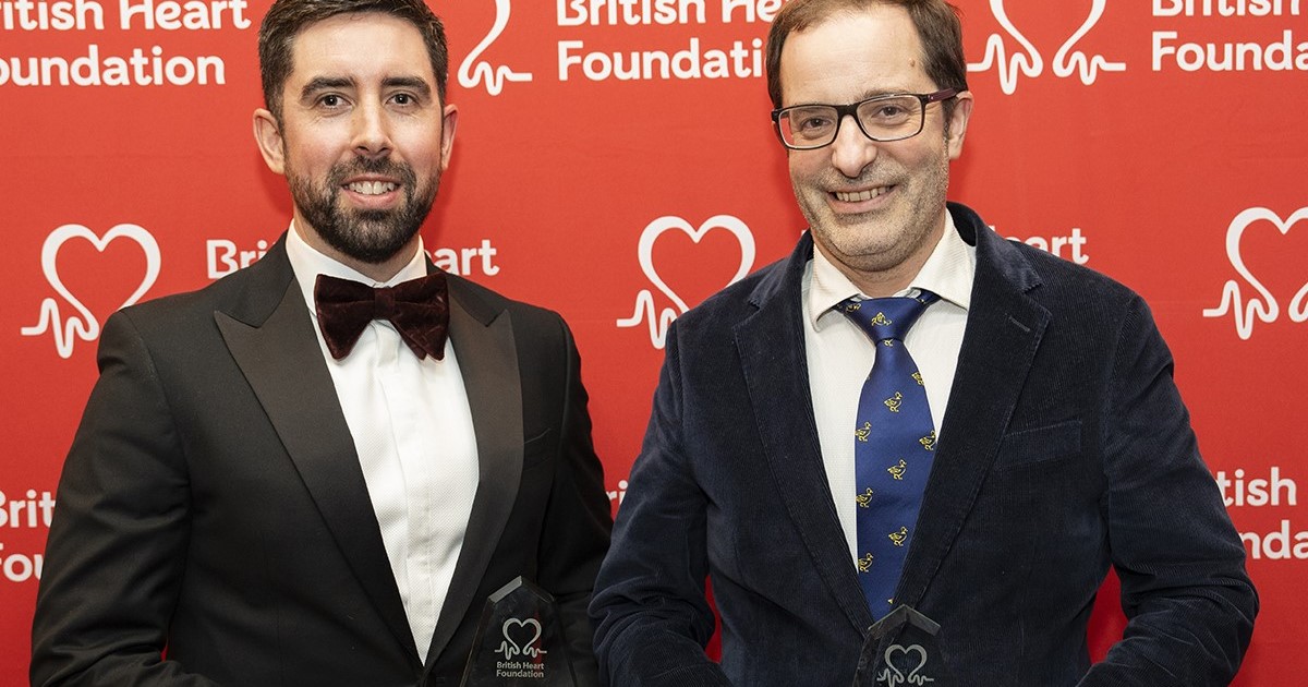 Dr Harry Pritchard and Professor Greenstein standing in front of a red background with white BHF logos