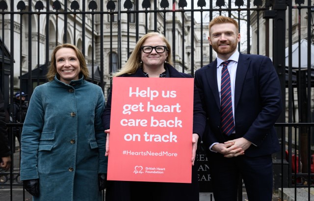 Helen Morgan MP, Dr Charmaine Griffiths, and Danny Beales MP stand outside the black iron gates of Downing Street. Charmaine is holding a red sign that says 'help us get heart care back on track'