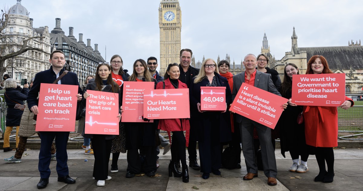A group of BHF campaigners holding red signs with white writing on them with various campaign slogans stand in front of Big Ben