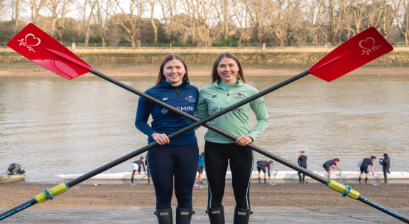 Image of two identical twins holding oars on the riverside