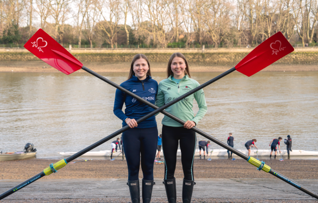 Image of identical twins Cathering and Gemma King holding oars on the riverside with rowers in the background 