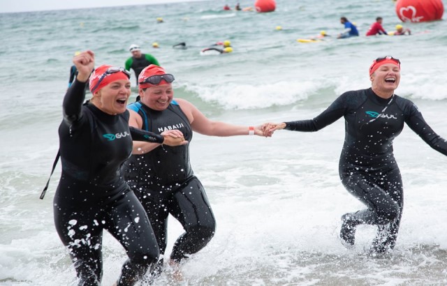 Three women in wet suits running out of the sea 