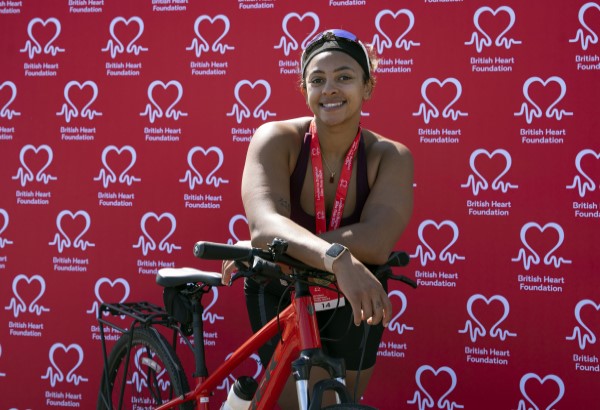 Image of BHF ambassador Ellie Downie leaning on bike smiling after completing BHF's London to Brighton Bike Ride