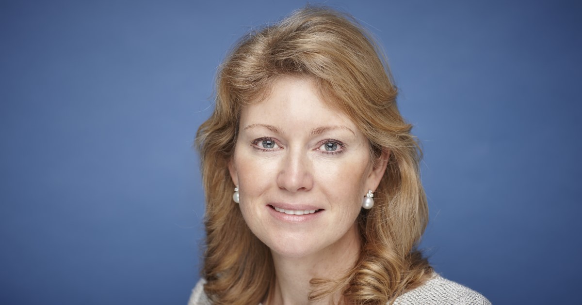 A photograph of of Karen Frank. She is pictured from the shoulders up against a blue background looking into the camera.