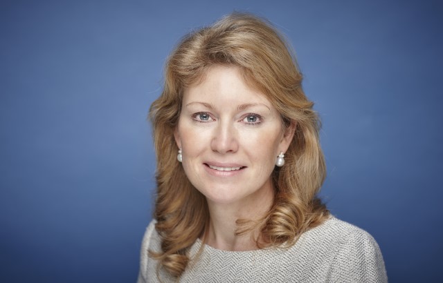 A photograph of of Karen Frank. She is pictured from the shoulders up against a blue background looking into the camera.