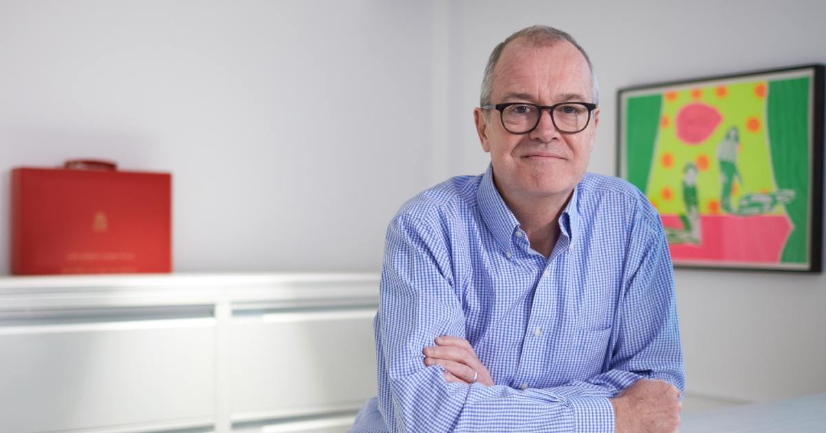 Sir Patrick Vallance leaning against a table, wearing a blue shirt.