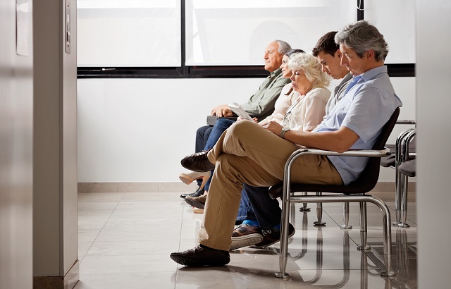 A stock photo of a row of people of various ages, genders and ethnicities sitting in a row of chairs all facing left