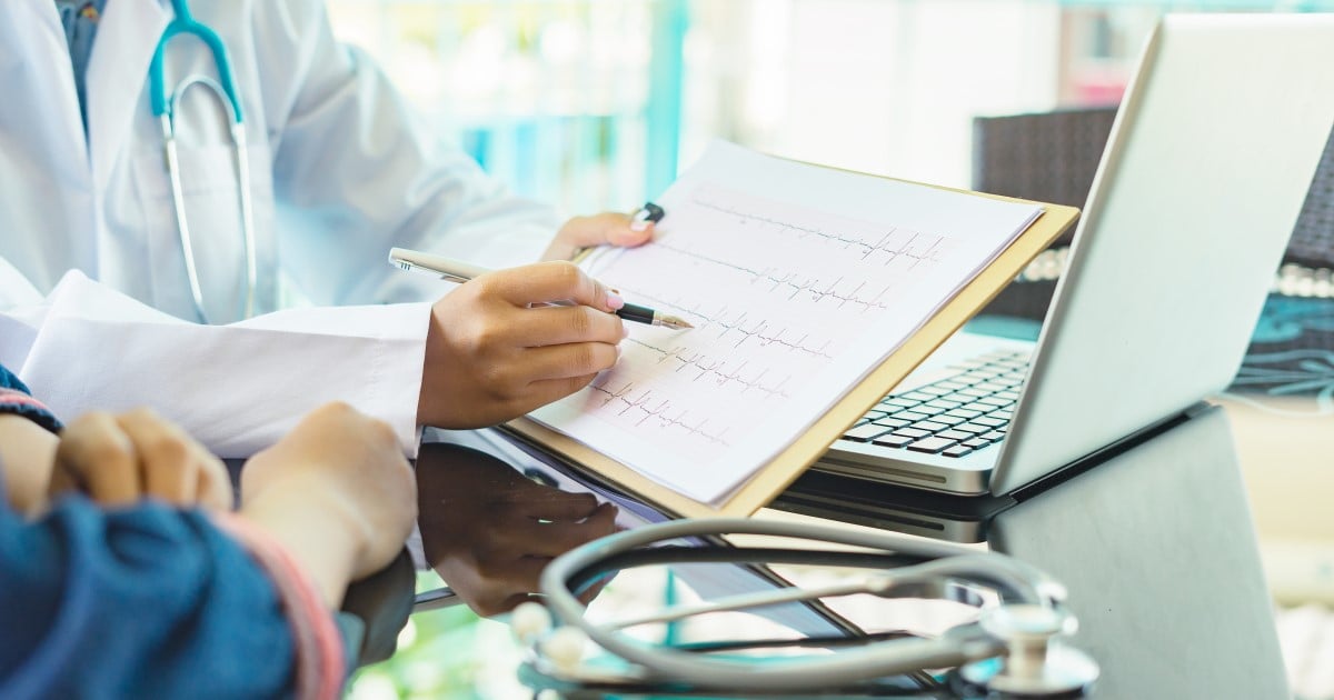 A doctor shows a patient ECG recordings on a piece of paper