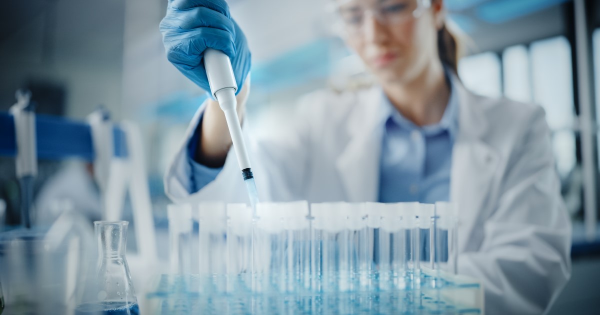 A woman in a lab coat pipettes liquid into a rack of test tubes