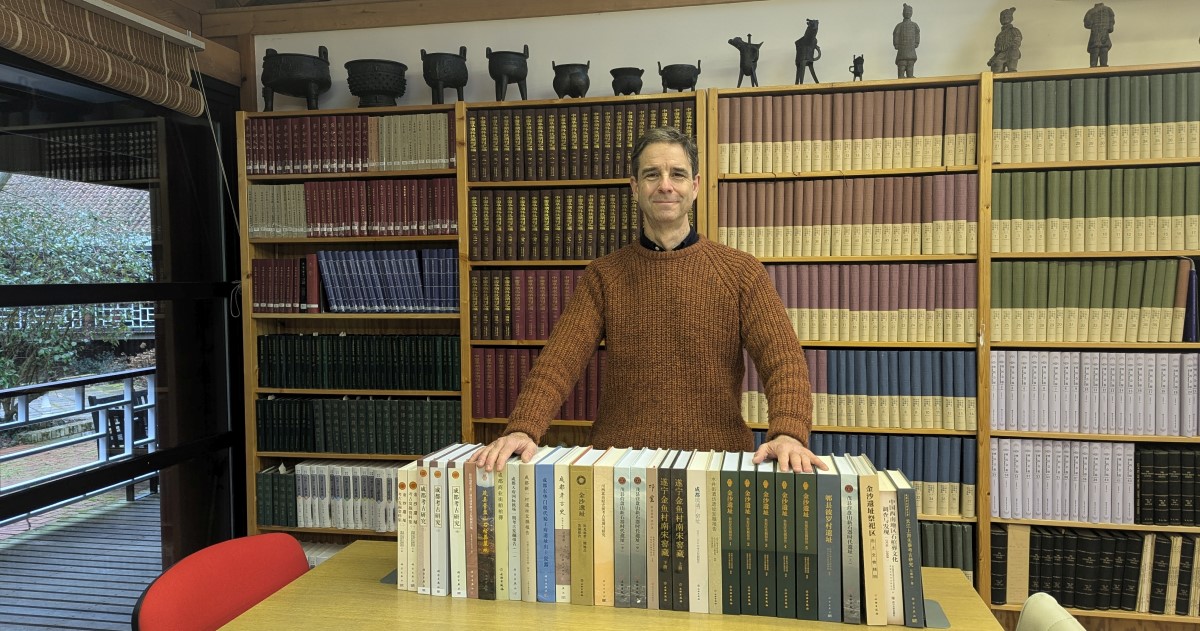 Trial participant John Moffett posses with a selection of books in front of a large bookcase 