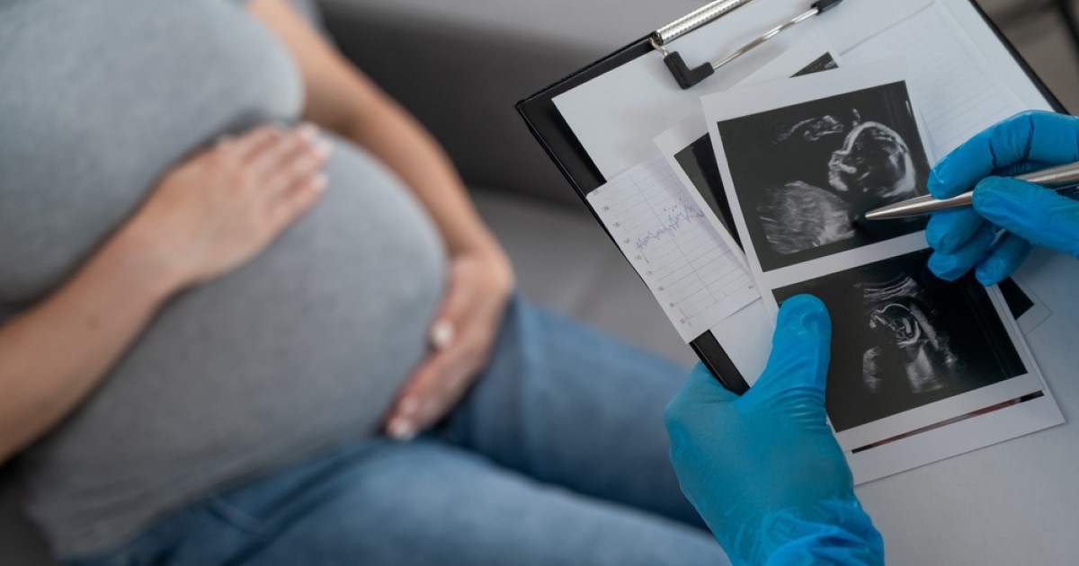 A pregnant woman holds her belly whilst a doctor examines ultrasound pictures of her baby